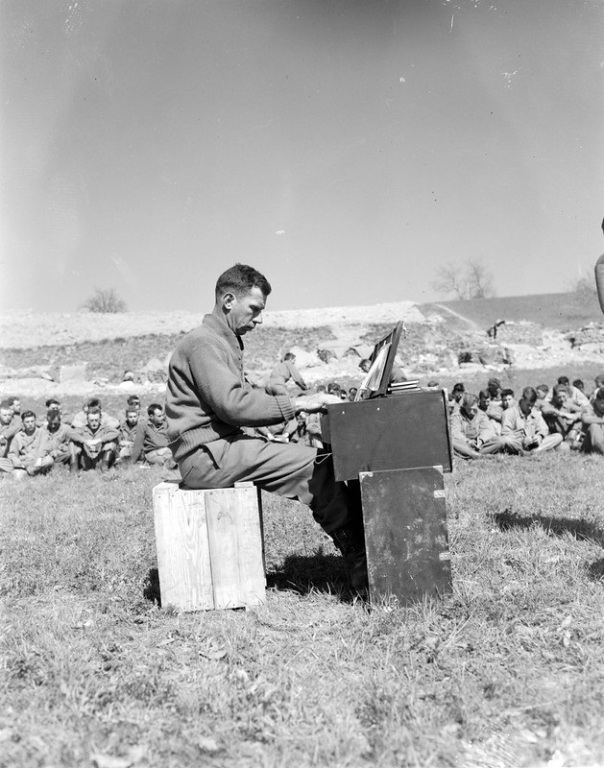 "Tenth Mountain Division Cpl. Ralph Squires plays the organ during the 605th Artillery Battalion Protestant Easter service held April 1, 1945, at Rocca Pitigliana, Italy. Worshipers sit on grass listening."
