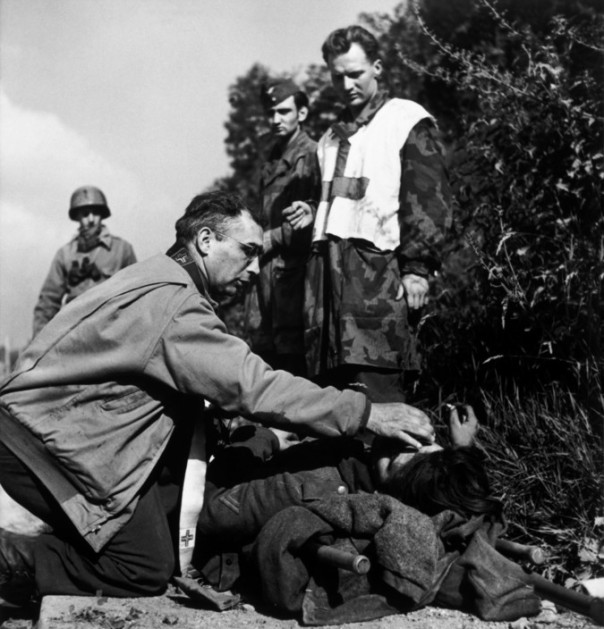 FRANCE. June/July, 1944. An American chaplain comforts a dying German soldier as prisoners of war look on.